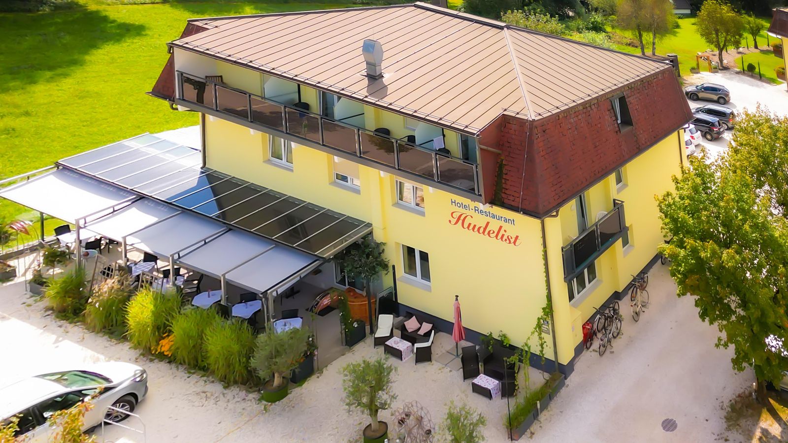 Das Hotel Hudelist von oben: gelbes Haus mit Balkonen, Gastgarten und Parkplatz im Grünen