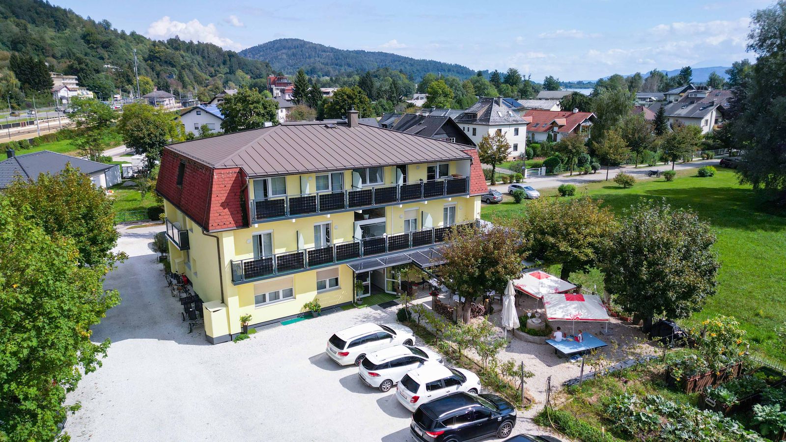 Das Hotel Hudelist aus der Vogelperspektive mit Parkplatz, Garten und Blick auf Krumpendorf