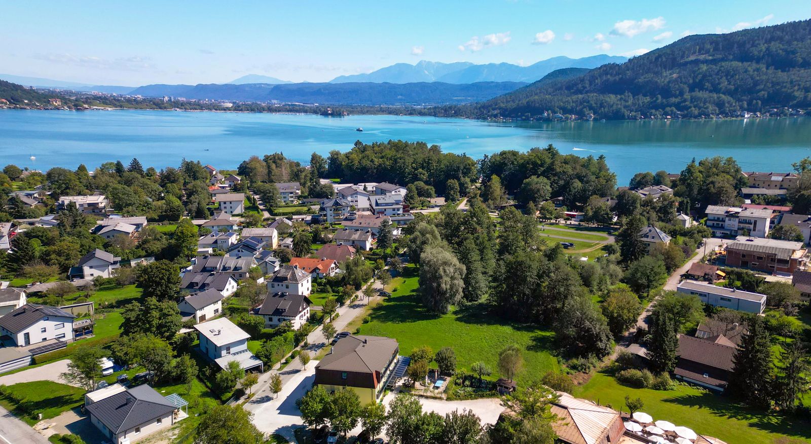 Luftaufnahme von Krumpendorf mit dem Hotel Hudelist im Vordergrund und dem Wörthersee samt Karawanken im Hintergrund