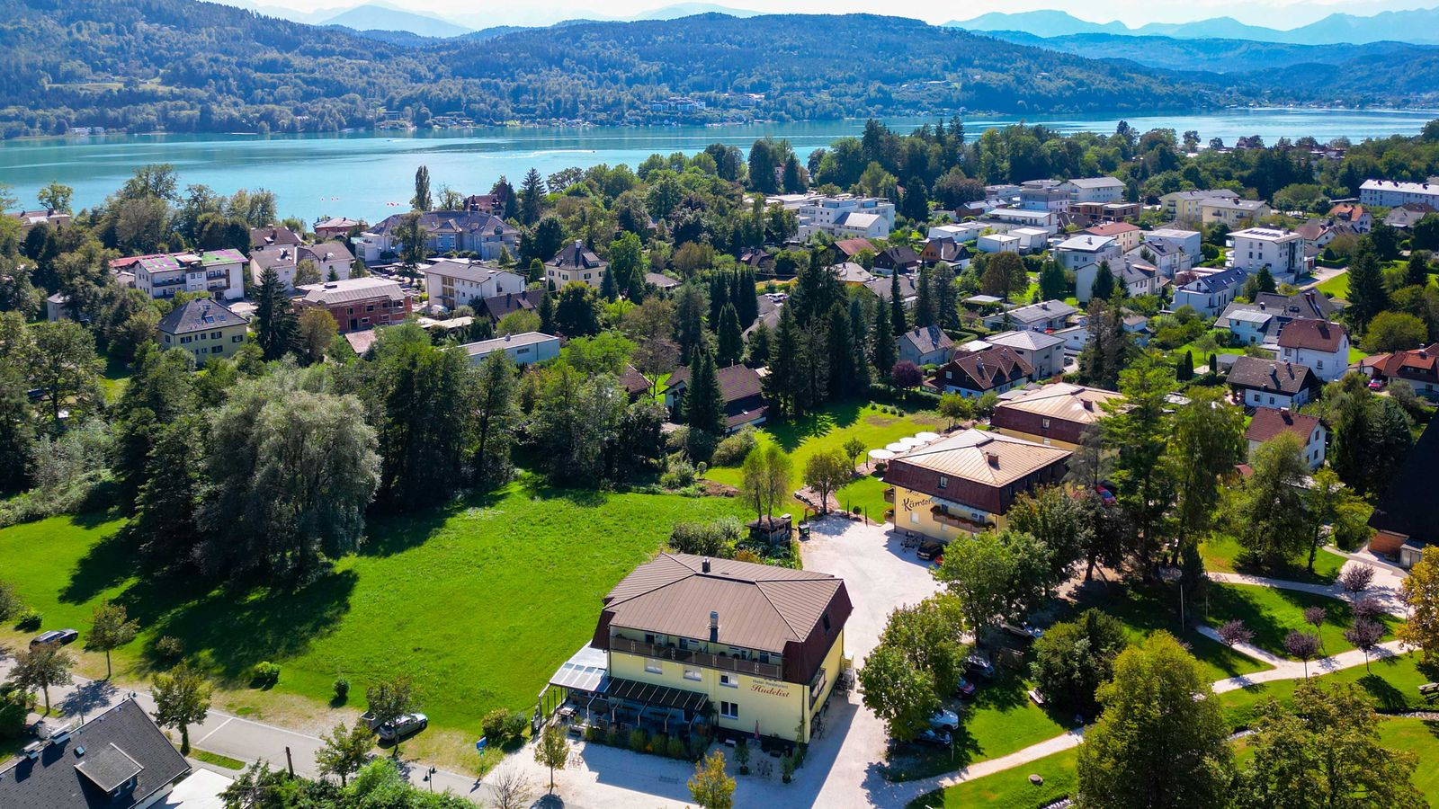 Luftaufnahme von Krumpendorf mit Parkanlagen, Hotel Hudelist und dem Wörthersee