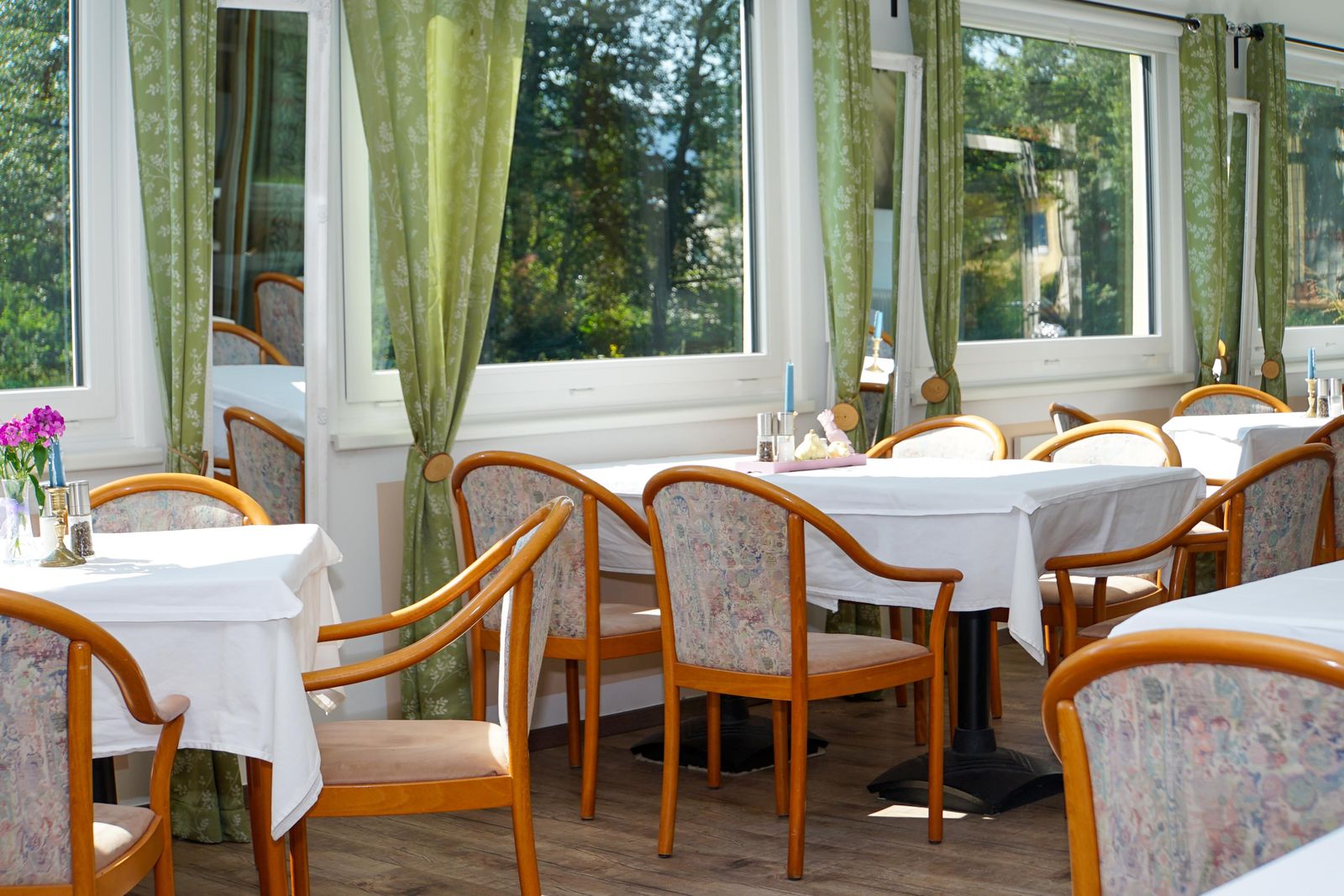 Heller Wintergarten des Restaurants mit weiß gedeckten Tischen und Blick ins Grüne