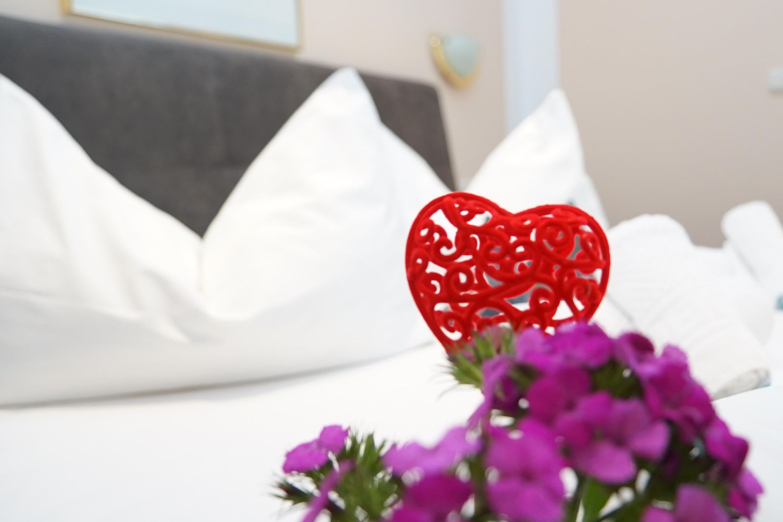 Liebevolle Dekoration mit Blumen und Herz auf dem Hotelbett